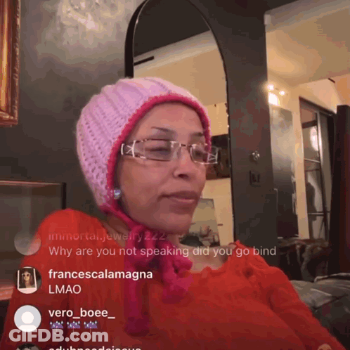 A Woman Wearing Glasses And A Pink Hat Is Sitting In Front Of A Mirror GIF