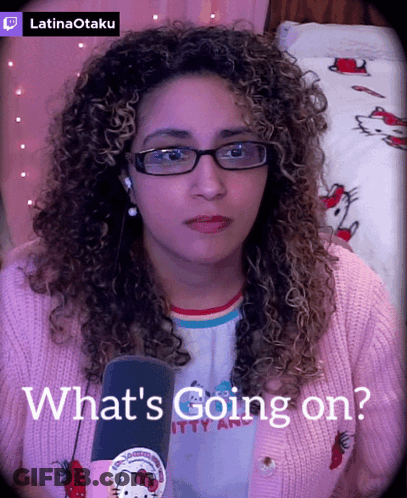 A Woman Wearing Glasses And A Pink Hello Kitty Sweater Says What 'S Going On In Front Of A Microphone GIF