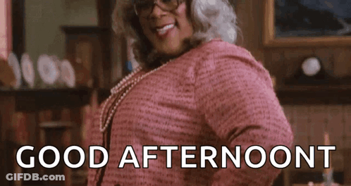 A Woman Wearing Glasses And A Pink Shirt Is Standing In A Living Room And Smiling . GIF