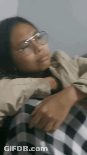 A Woman Wearing Glasses And A Plaid Shirt Is Laying Down GIF
