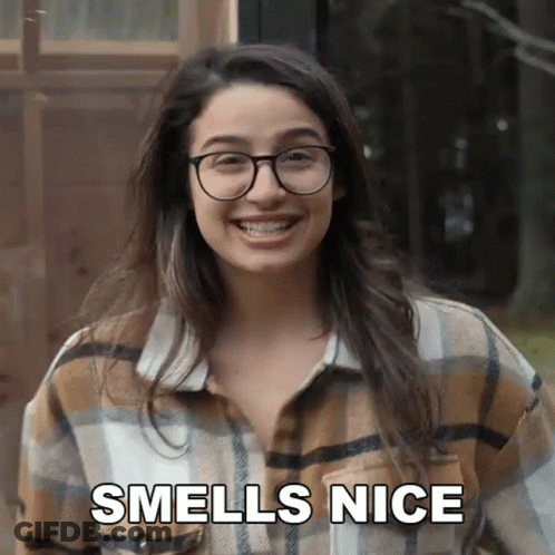 A Woman Wearing Glasses And A Plaid Shirt Smiles And Says " Smells Nice " GIF