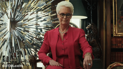A Woman Wearing Glasses And A Red Shirt Is Sitting In Front Of A Display Of Knives GIF