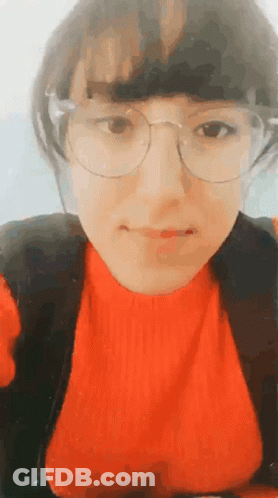A Woman Wearing Glasses And A Red Sweater Looks At The Camera GIF
