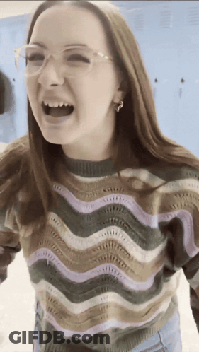 A Woman Wearing Glasses And A Striped Sweater Is Laughing With Her Mouth Open GIF