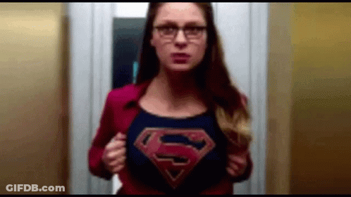 A Woman Wearing Glasses And A Superman Cape Is Standing In An Elevator . GIF