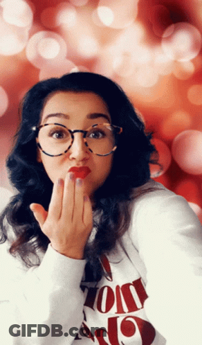 A Woman Wearing Glasses And A Sweater That Says ' I Love You ' On It Blows A Kiss GIF