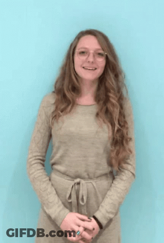 A Woman Wearing Glasses And A Tan Dress Is Smiling GIF