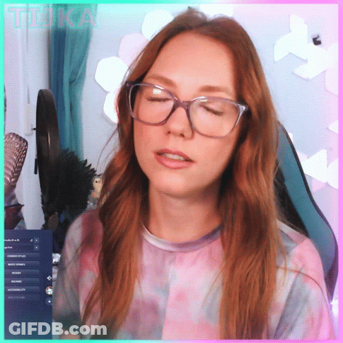 A Woman Wearing Glasses And A Tie Dye Shirt Is Sitting In Front Of A Computer Screen With The Word Tika Written On It GIF