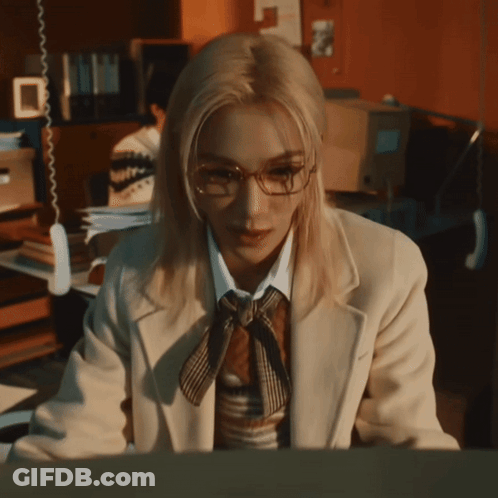 A Woman Wearing Glasses And A Tie Is Sitting In Front Of A Computer GIF