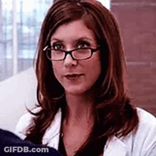 A Woman Wearing Glasses And A White Coat Is Sitting In Front Of A Window . GIF