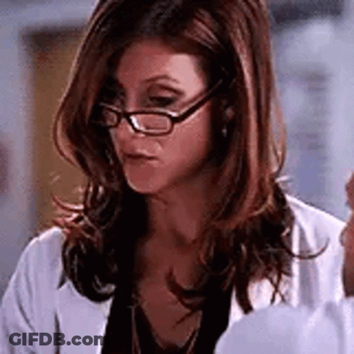 A Woman Wearing Glasses And A White Lab Coat Is Looking Down . GIF