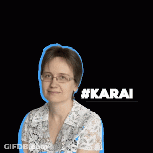 A Woman Wearing Glasses And A White Shirt Stands In Front Of A Sign That Says #Karai GIF