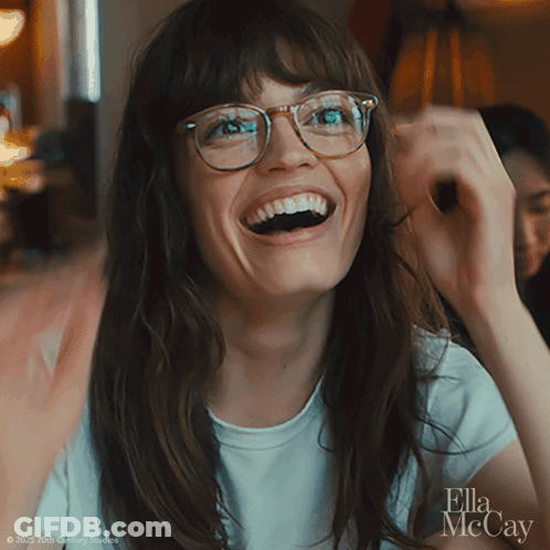 A Woman Wearing Glasses And A White Shirt With Ella Mccay On The Bottom Right GIF