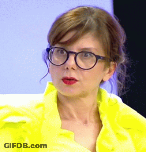 A Woman Wearing Glasses And A Yellow Jacket Is Making A Funny Face . GIF
