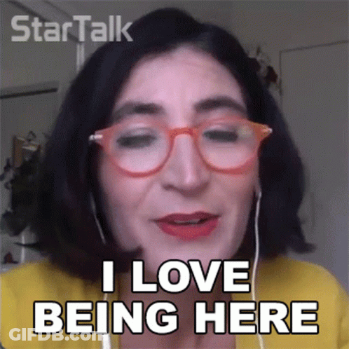 A Woman Wearing Glasses And Ear Buds Says I Love Being Here GIF