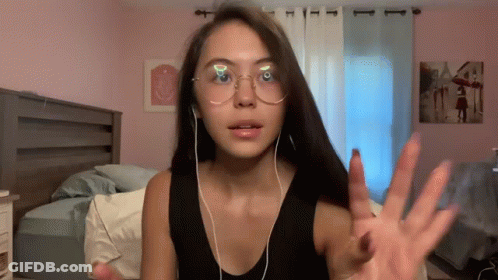 A Woman Wearing Glasses And Ear Buds Shows Her Hand GIF