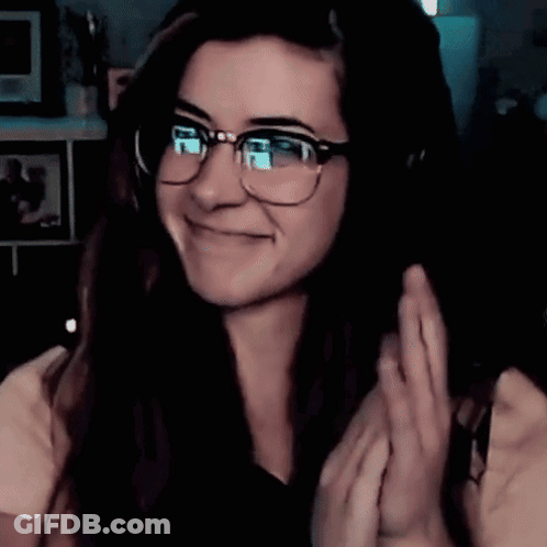 A Woman Wearing Glasses And Headphones Is Smiling And Waving GIF