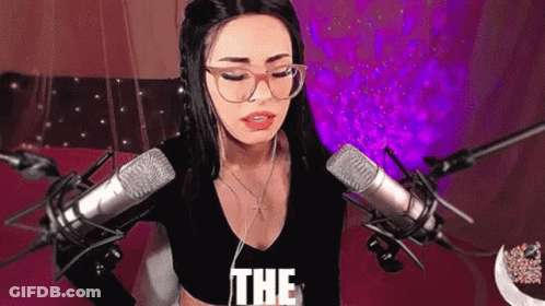 A Woman Wearing Glasses And Headphones Is Standing In Front Of A Microphone And Says The . GIF