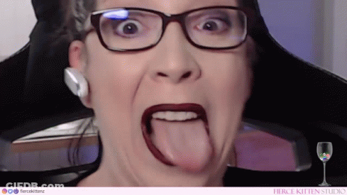 A Woman Wearing Glasses And Red Lipstick Is Sticking Her Tongue Out . GIF