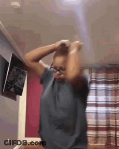 A Woman Wearing Glasses Is Dancing In A Room With Her Hands In Her Hair . GIF