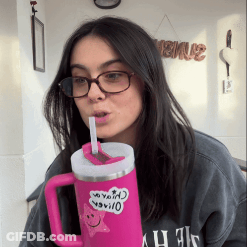 A Woman Wearing Glasses Is Drinking From A Pink Mug With A Sticker On It That Says " I Love You " On It GIF