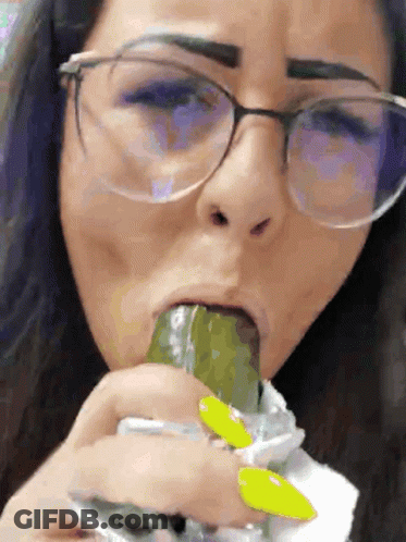 A Woman Wearing Glasses Is Eating A Pickle With Her Tongue GIF