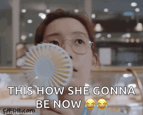 A Woman Wearing Glasses Is Holding A Fan In Her Mouth And Says This How She Gonna Be Now GIF