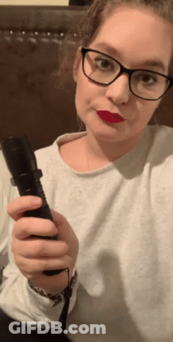 A Woman Wearing Glasses Is Holding A Flashlight In Her Hand GIF