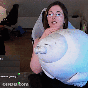 A Woman Wearing Glasses Is Holding A Stuffed Seal In Her Hands GIF