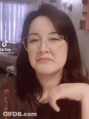 A Woman Wearing Glasses Is Making A Funny Face And Looking At The Camera . GIF