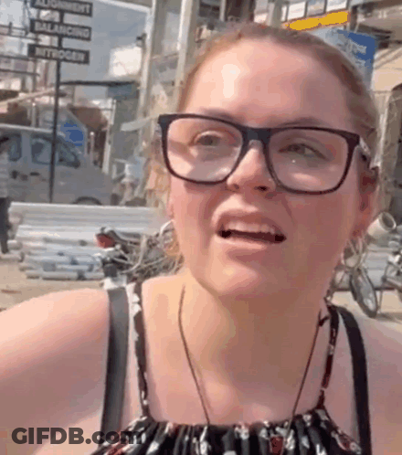 A Woman Wearing Glasses Is Making A Funny Face In Front Of A Sign That Says Balance GIF