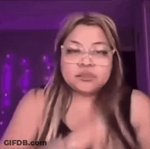 A Woman Wearing Glasses Is Making A Funny Face While Standing In Front Of A Purple Wall . GIF