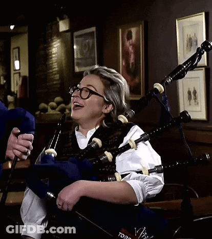 A Woman Wearing Glasses Is Playing A Bagpipe In A Room With Pictures On The Wall GIF