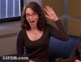 A Woman Wearing Glasses Is Sitting At A Table And Waving Her Hand . GIF