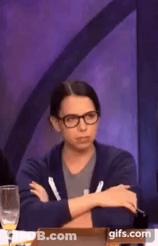 A Woman Wearing Glasses Is Sitting At A Table With Her Arms Crossed And A Glass Of Wine . GIF