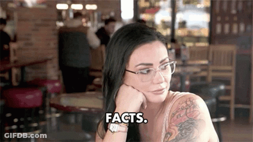 A Woman Wearing Glasses Is Sitting At A Table With Her Hand On Her Chin And Says Facts . GIF