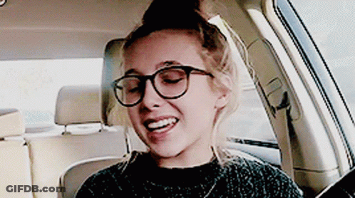 A Woman Wearing Glasses Is Sitting In A Car And Smiling GIF