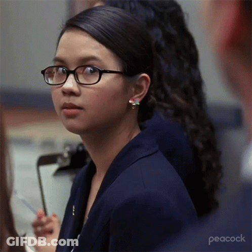 A Woman Wearing Glasses Is Sitting In Front Of A Clipboard With Peacock Written On The Bottom GIF