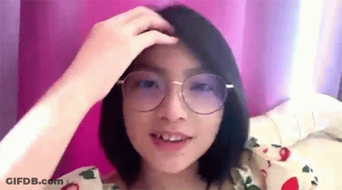 A Woman Wearing Glasses Is Sitting On A Bed . GIF