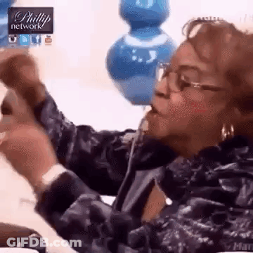 A Woman Wearing Glasses Is Sitting On A Couch And Eating A Piece Of Food . GIF