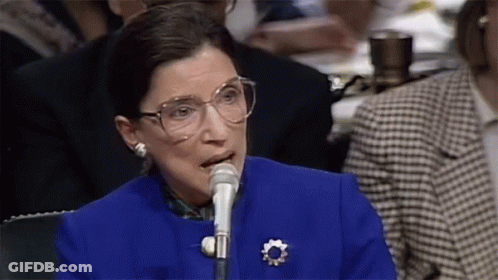 A Woman Wearing Glasses Is Speaking Into A Microphone GIF