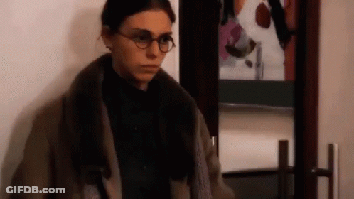 A Woman Wearing Glasses Is Standing In Front Of A Door . GIF
