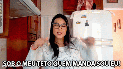 A Woman Wearing Glasses Is Standing In Front Of A Refrigerator With Sob O Meu Teto Quem Manda Sou Eu Written On It GIF