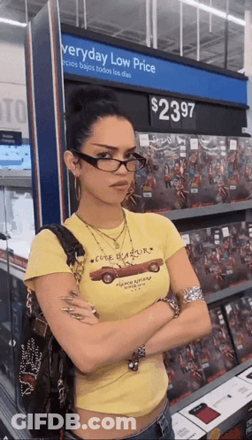 A Woman Wearing Glasses Is Standing In Front Of A Sign That Says Everyday Low Price GIF