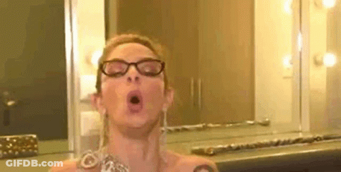 A Woman Wearing Glasses Is Taking A Selfie In Front Of A Mirror In A Room . GIF