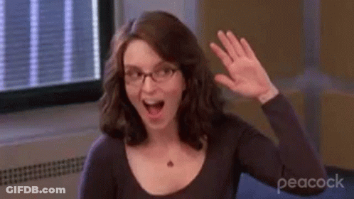 A Woman Wearing Glasses Is Waving Her Hand In Front Of A Window In A Room . GIF