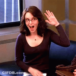 A Woman Wearing Glasses Is Waving Her Hand While Sitting On A Couch GIF