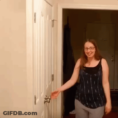 A Woman Wearing Glasses Opens A Door In A Room GIF