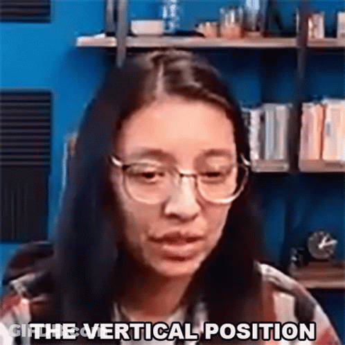 A Woman Wearing Glasses Says The Vertical Position In Front Of A Bookshelf . GIF