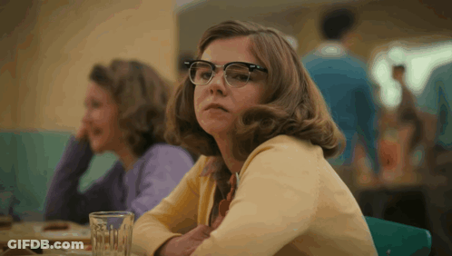 A Woman Wearing Glasses Sits At A Table With A Glass Of Water In Front Of Her GIF